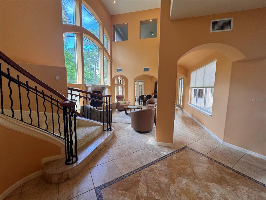 A two-story living room features a grand staircase, floor-to-ceiling windows, and tile flooring — 779 E CHAPMAN ROAD, OVIEDO, FL