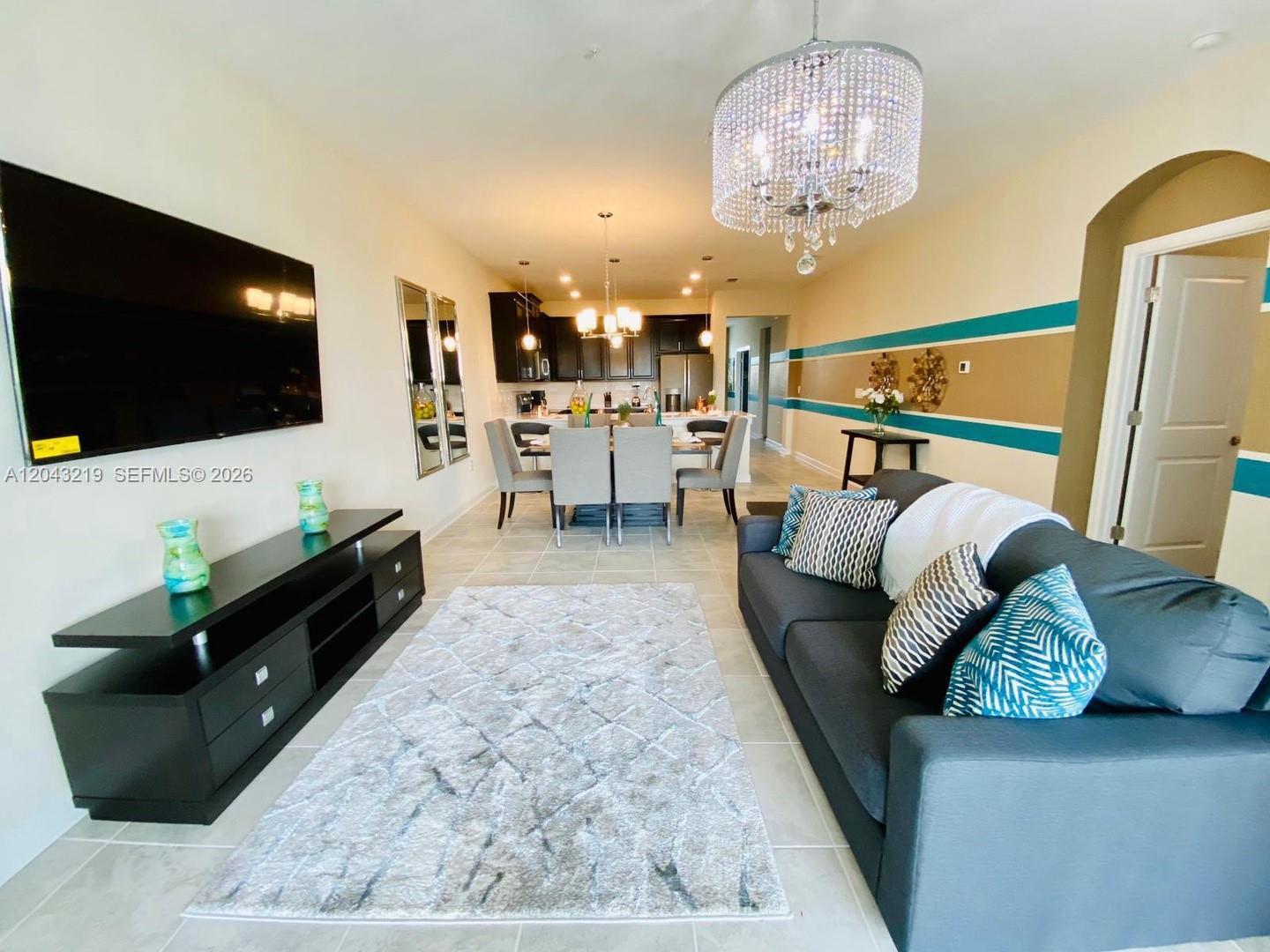 A living room with a dark sofa, television, and dining area with a crystal chandelier — 655 Ocean Course # 0, Davenport FL 33896, DAVENPORT, FL