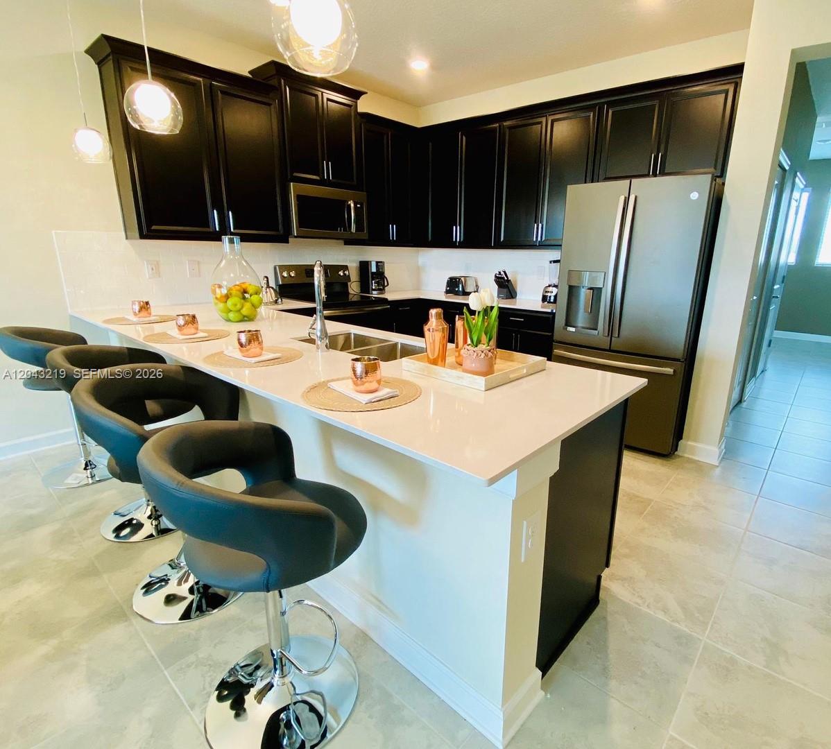 A modern kitchen features dark cabinetry, white countertops, a breakfast bar, and stainless steel appliances — 655 Ocean Course # 0, Davenport FL 33896, DAVENPORT, FL