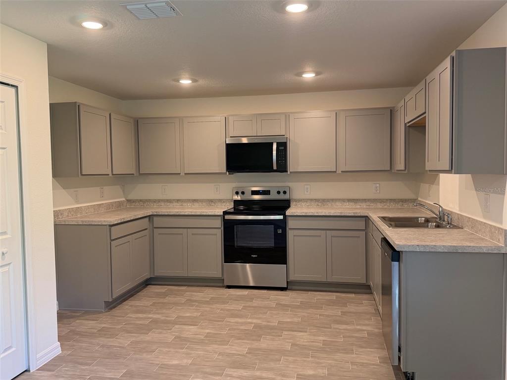 A kitchen features gray shaker-style cabinets, stainless steel appliances, and light-colored laminate countertops — 904 HUDSON VALLEY DRIVE, POINCIANA, FL