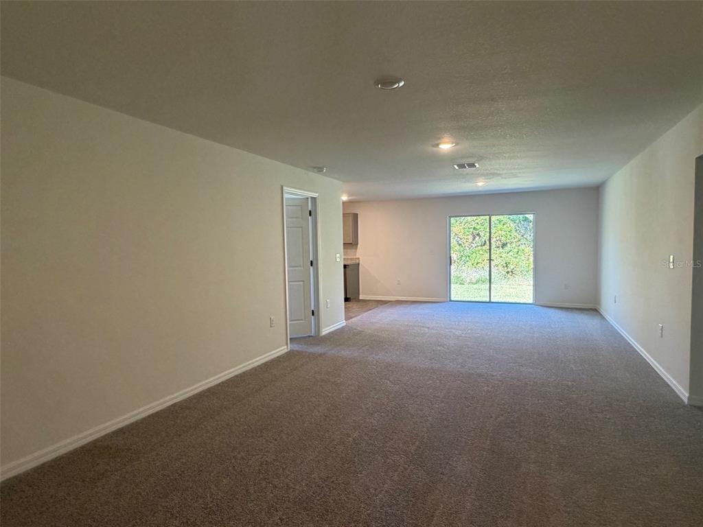 An empty living room features beige carpeting, white walls, a doorway, and sliding glass doors — 904 HUDSON VALLEY DRIVE, POINCIANA, FL