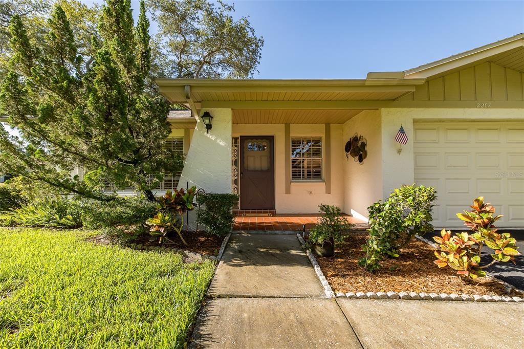 A single-story house exterior features a covered entryway, a brown front door, and a garage — 2207 MARSHALL DRIVE, DUNEDIN, FL