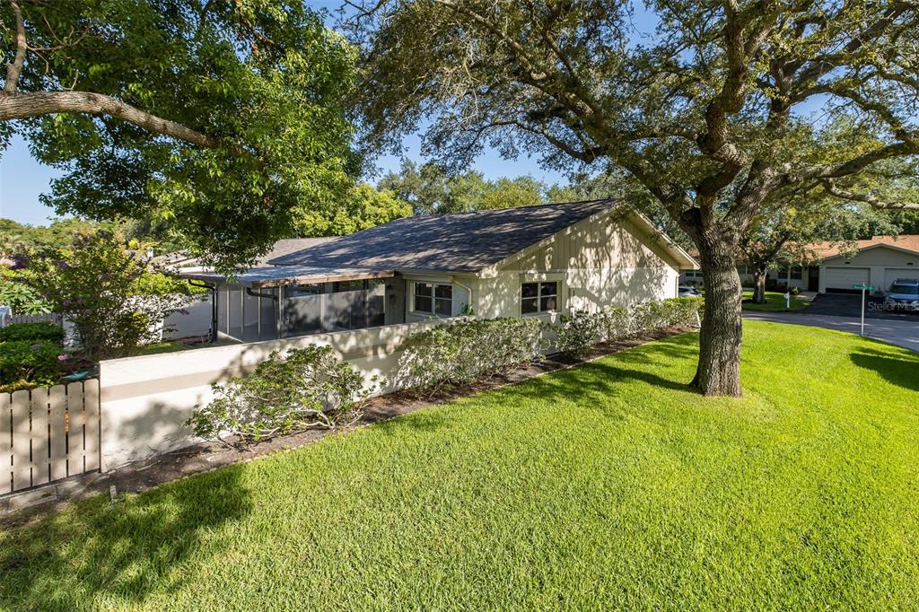 A single-story house exterior features a screened-in patio, a low stucco wall, and mature trees — 2207 MARSHALL DRIVE, DUNEDIN, FL