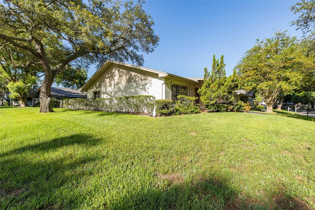 A single-story house with a light-colored exterior sits on a grassy lawn with large trees — 2207 MARSHALL DRIVE, DUNEDIN, FL