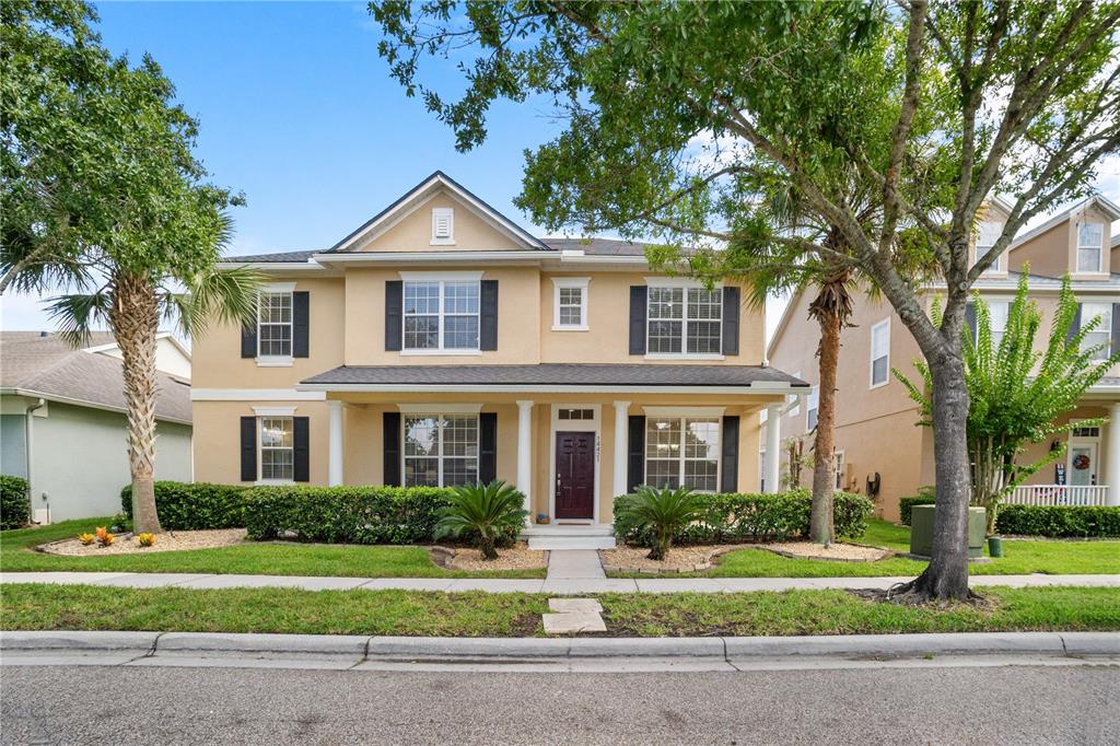 A two-story tan house with black shutters, a covered front porch, and a landscaped yard — 14421 PARADISE TREE DRIVE, ORLANDO, FL