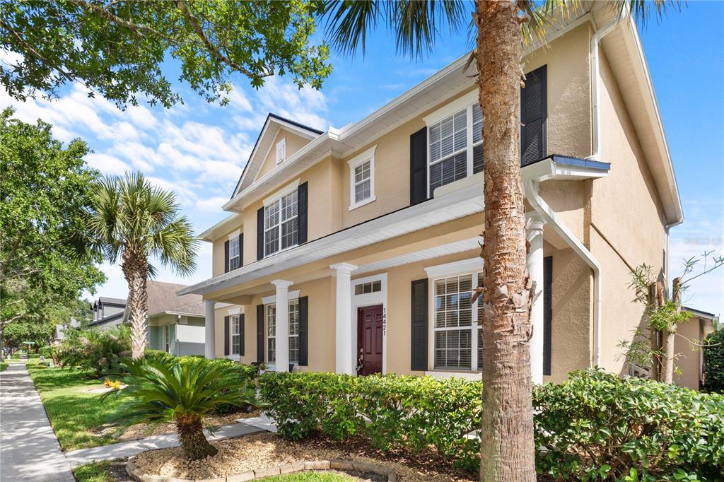 A two-story tan house with a front porch, dark shutters, and a palm tree — 14421 PARADISE TREE DRIVE, ORLANDO, FL