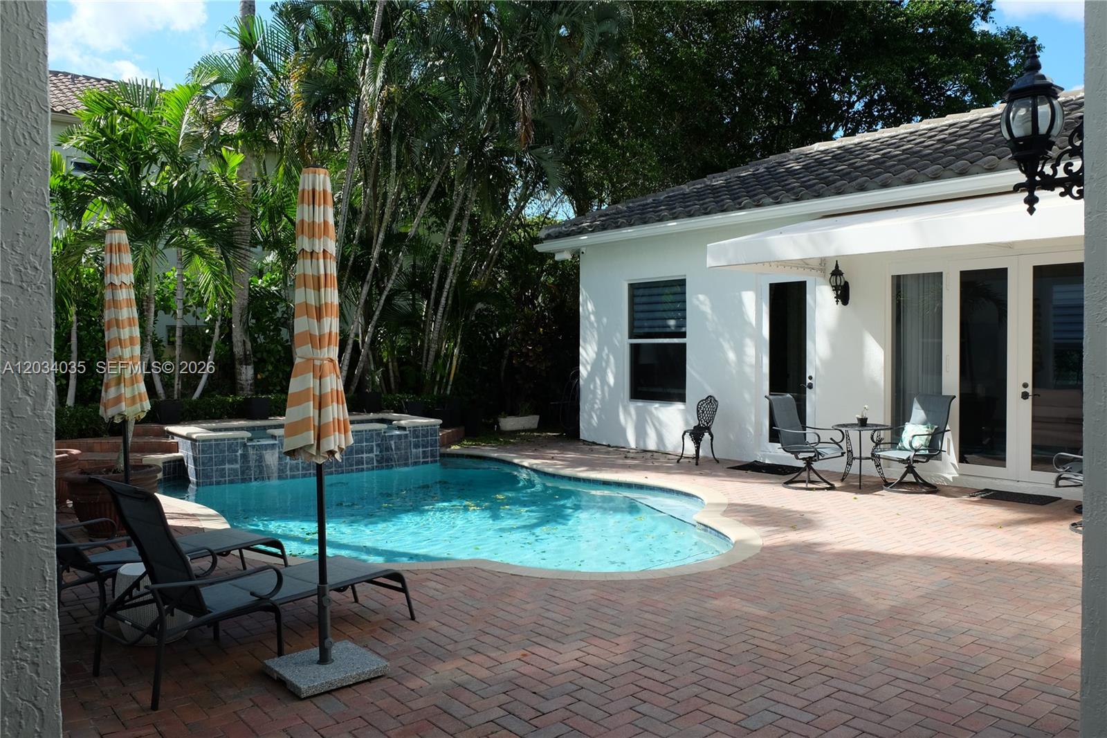 A backyard patio features a swimming pool, lounge chairs, umbrellas, and a white house exterior — 375 SW 16th St # 1, Boca Raton FL 33432, BOCA RATON, FL