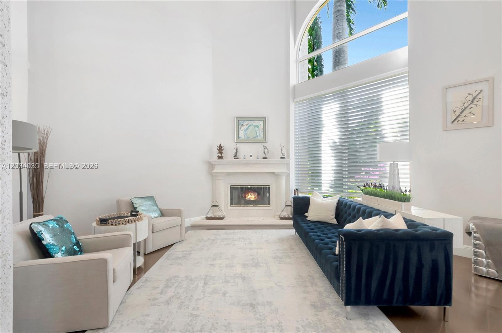 A bright living room features a fireplace, a blue tufted sofa, and large arched windows — 375 SW 16th St # 1, Boca Raton FL 33432, BOCA RATON, FL