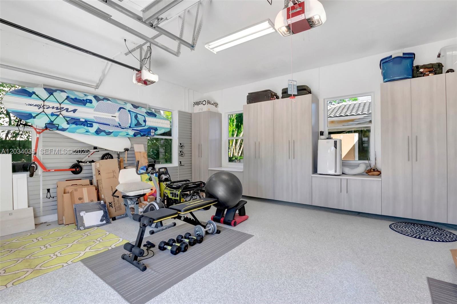 A garage with light-colored cabinetry, a gym area, and a paddleboard mounted on the wall — 375 SW 16th St # 1, Boca Raton FL 33432, BOCA RATON, FL
