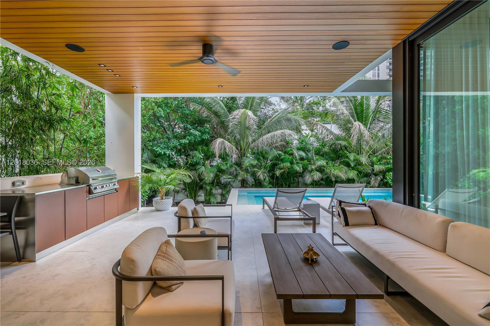 A covered outdoor patio features a kitchen, lounge seating, and a pool surrounded by greenery — 1092 N Venetian Dr, Miami FL 33139, MIAMI, FL