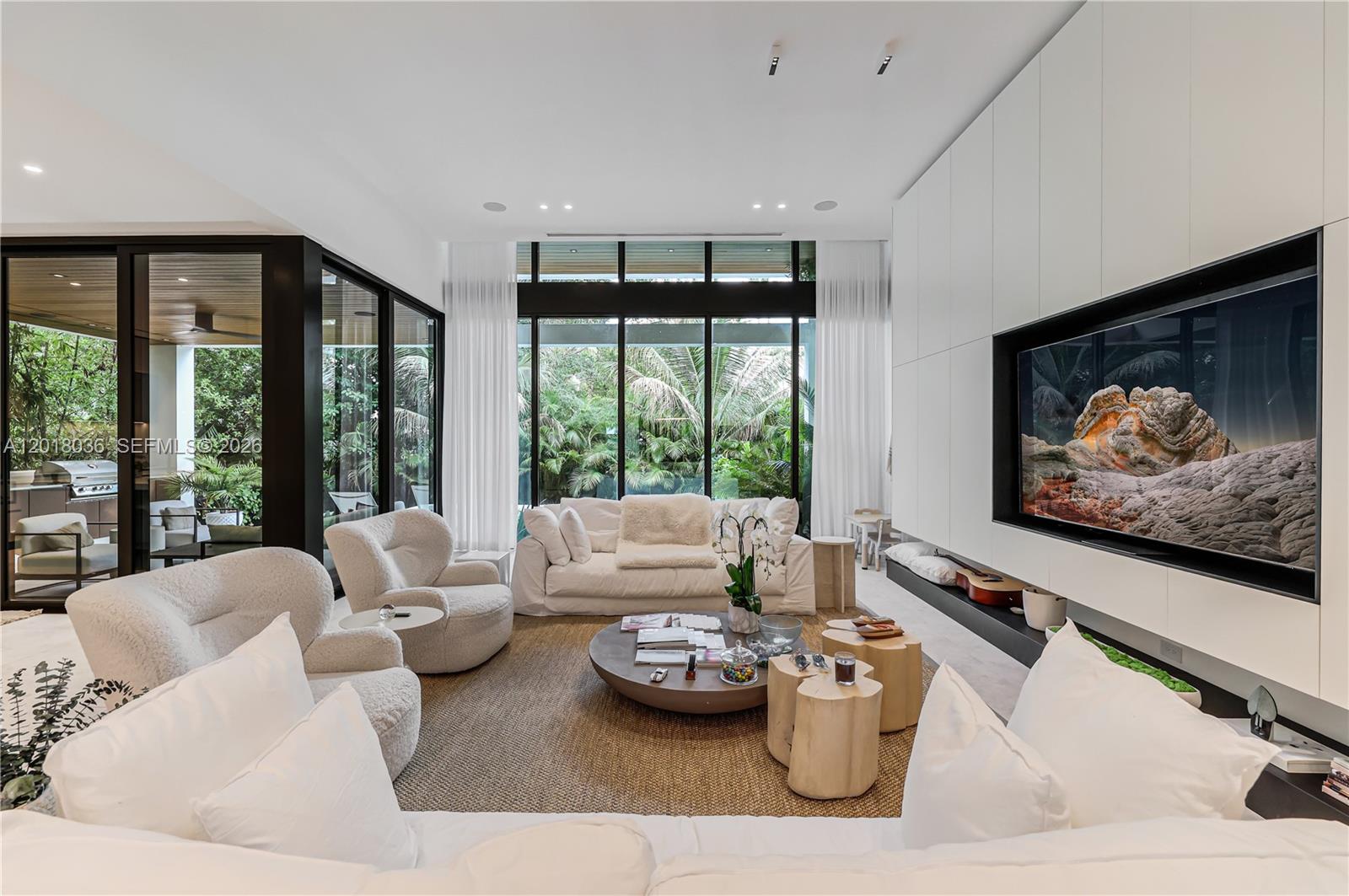 A modern living room features white furniture, a large television, and floor-to-ceiling windows — 1092 N Venetian Dr, Miami FL 33139, MIAMI, FL