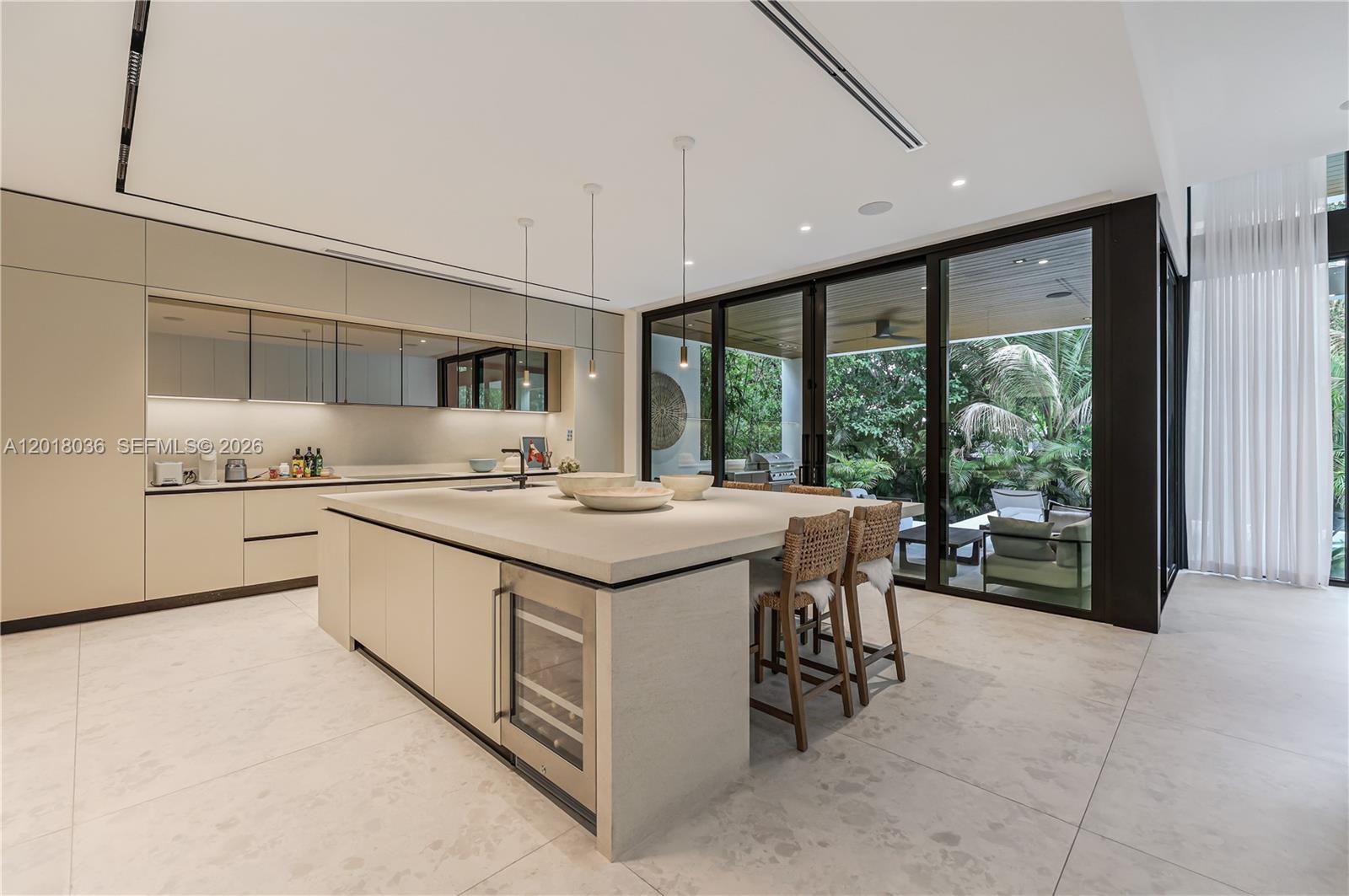 A modern kitchen features a large stone island, light cabinetry, and floor-to-ceiling glass doors — 1092 N Venetian Dr, Miami FL 33139, MIAMI, FL