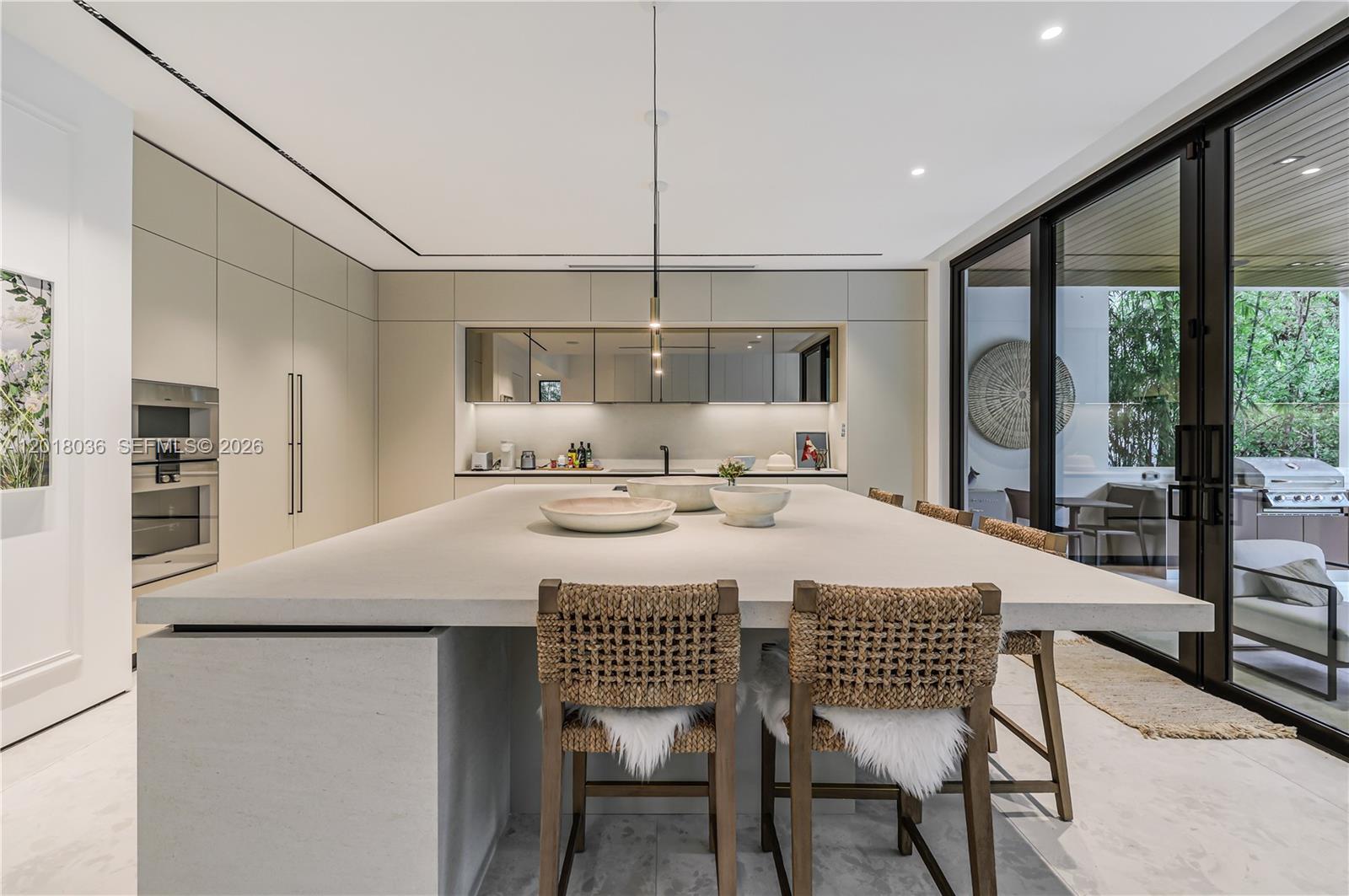 A modern kitchen features a large stone island, woven bar stools, and floor-to-ceiling cabinetry — 1092 N Venetian Dr, Miami FL 33139, MIAMI, FL