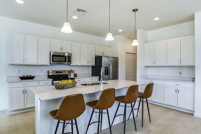 A modern kitchen features white cabinets, a large island with bar stools, and stainless steel appliances — 2626 HAM BROWN ROAD UNIT Magdalena, KISSIMMEE, FL