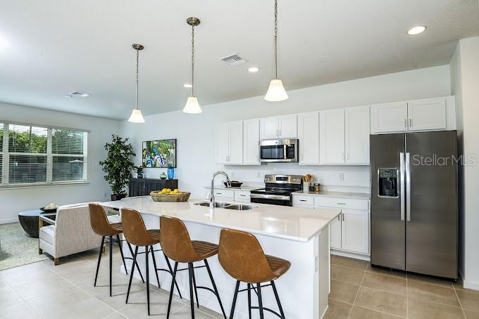 A modern kitchen features white cabinetry, stainless steel appliances, and a central island with bar stools — 2626 HAM BROWN ROAD UNIT Magdalena, KISSIMMEE, FL