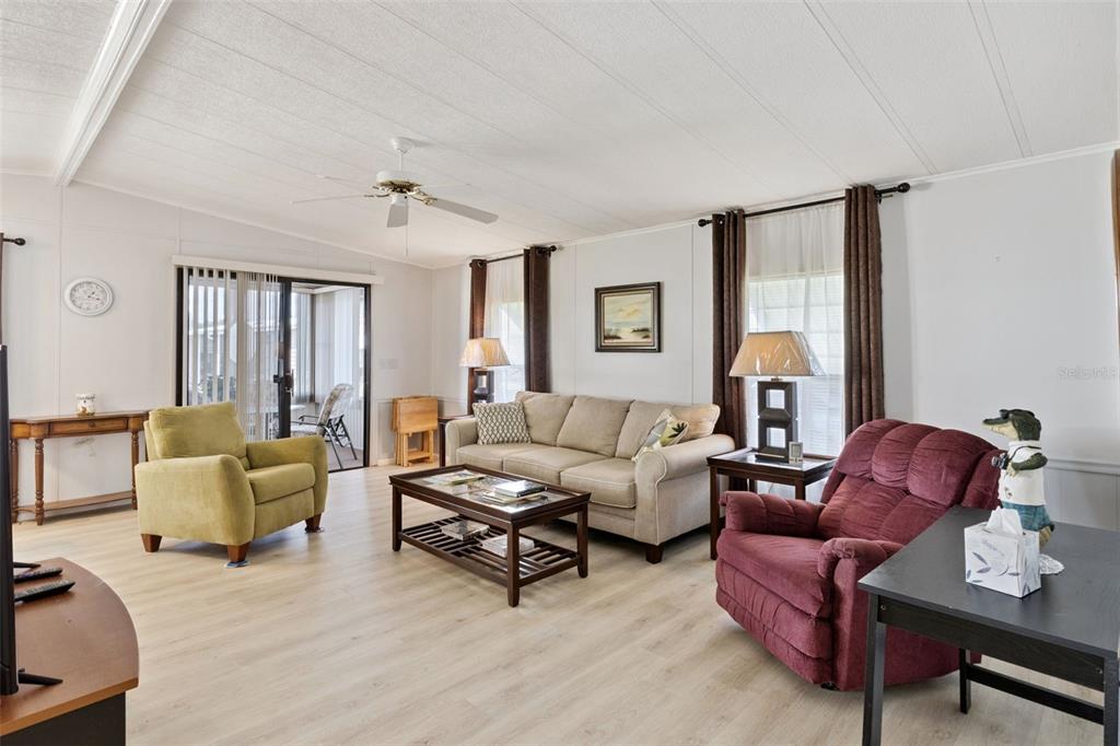 A living room features light wood-look flooring, a beige sofa, and a maroon recliner — 125 LAKE HAZEL DRIVE, WINTER HAVEN, FL
