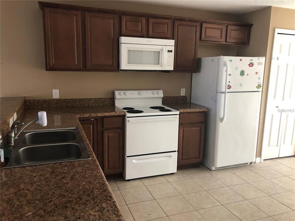 A kitchen features dark wood cabinets, granite countertops, white appliances, and light tile flooring — 325 BACCARAT COURT UNIT B, KISSIMMEE, FL