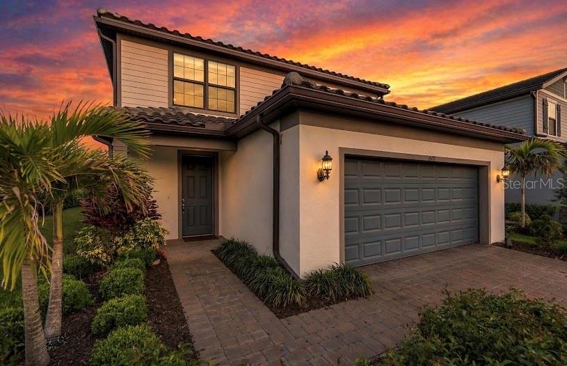 A two-story house with a gray garage, a paved walkway, and a palm tree at sunset — 6111 BLUESTAR COURT, BRADENTON, FL