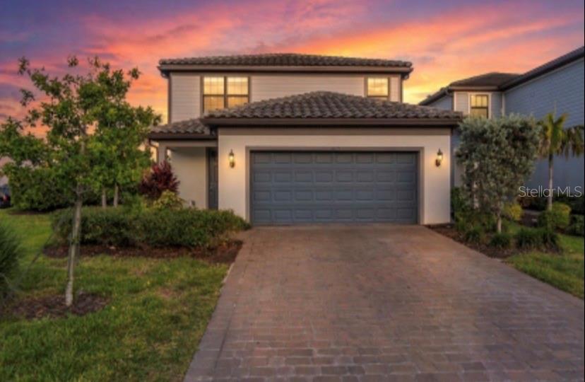A two-story house with a tiled roof, a gray garage door, and a brick driveway — 6111 BLUESTAR COURT, BRADENTON, FL