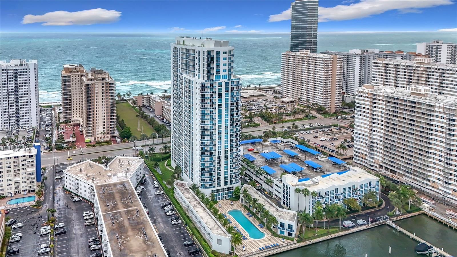 An aerial view shows a tall residential tower surrounded by parking structures and a pool — 1945 S Ocean Dr # 605, Hallandale Beach FL 33009, HALLANDALE BEACH, FL