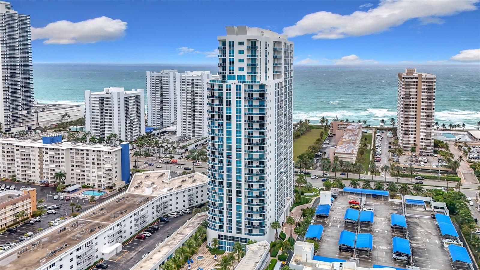 An aerial view shows a tall residential skyscraper surrounded by other buildings and parking lots — 1945 S Ocean Dr # 605, Hallandale Beach FL 33009, HALLANDALE BEACH, FL