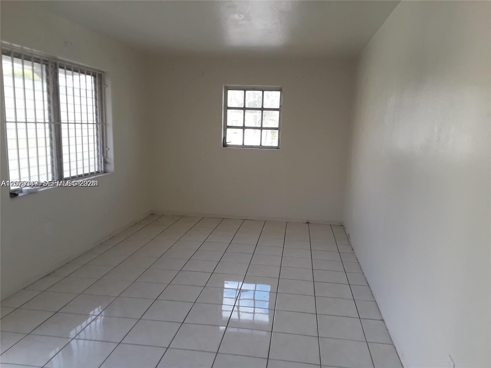 An empty room features white walls, white tile flooring, and two windows with security bars — 236 Madeira Ave # 6, Coral Gables FL 33134, CORAL GABLES, FL
