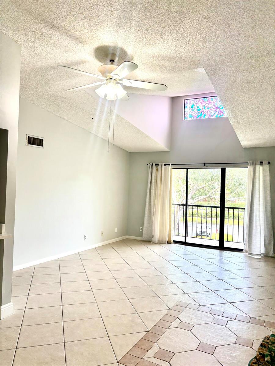 A living room with vaulted ceilings, a ceiling fan, tile flooring, and a sliding glass door — 201 Foxtail Drive # H3, FL 33415, FL