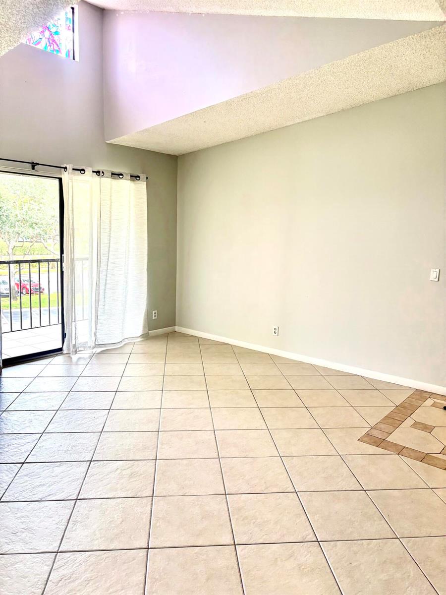 A living room with light-colored walls, tile flooring, a vaulted ceiling, and a sliding glass door — 201 Foxtail Drive # H3, FL 33415, FL