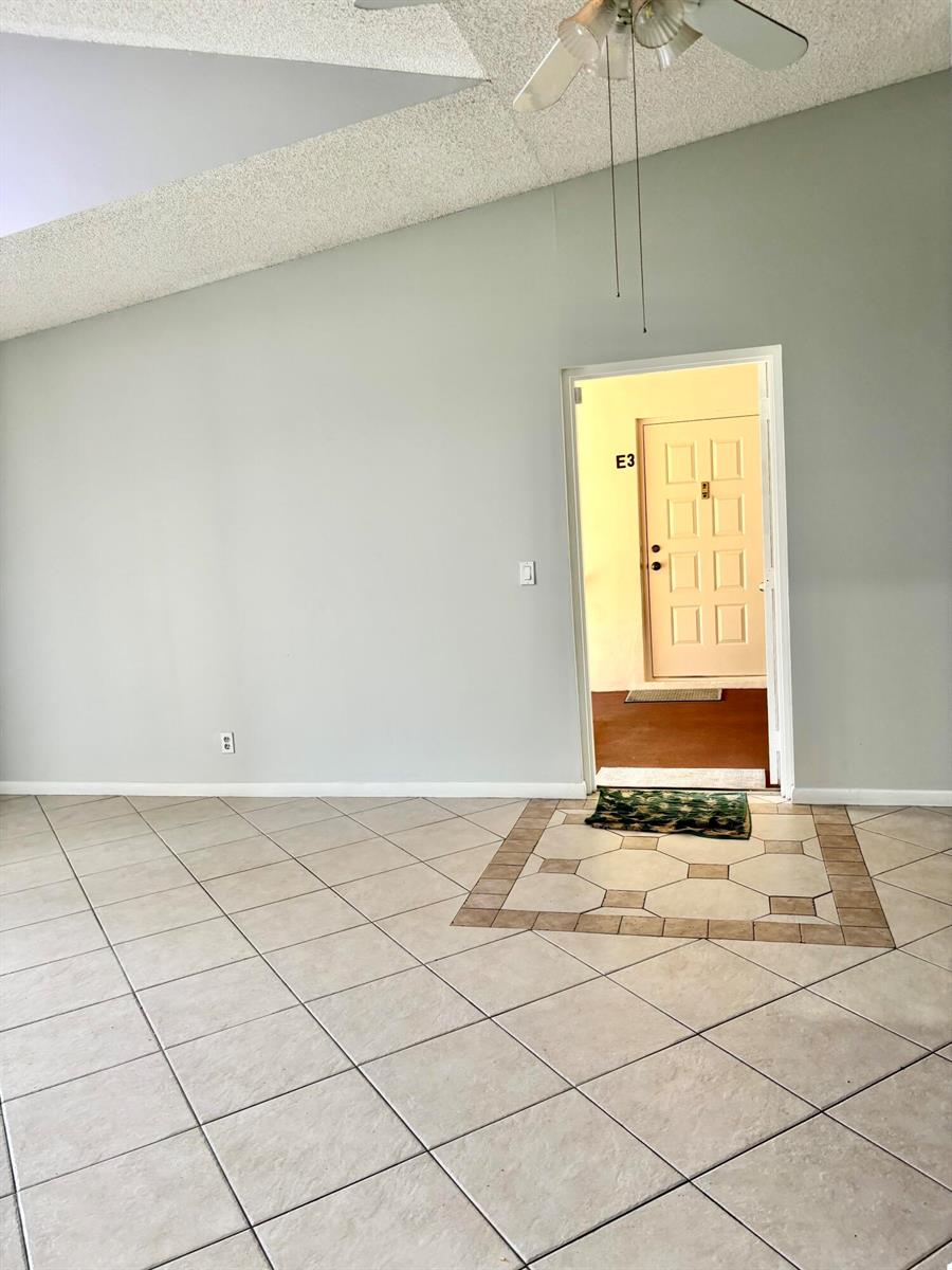 A room with light-colored tile flooring, a vaulted ceiling, and a doorway leading outside — 201 Foxtail Drive # H3, FL 33415, FL