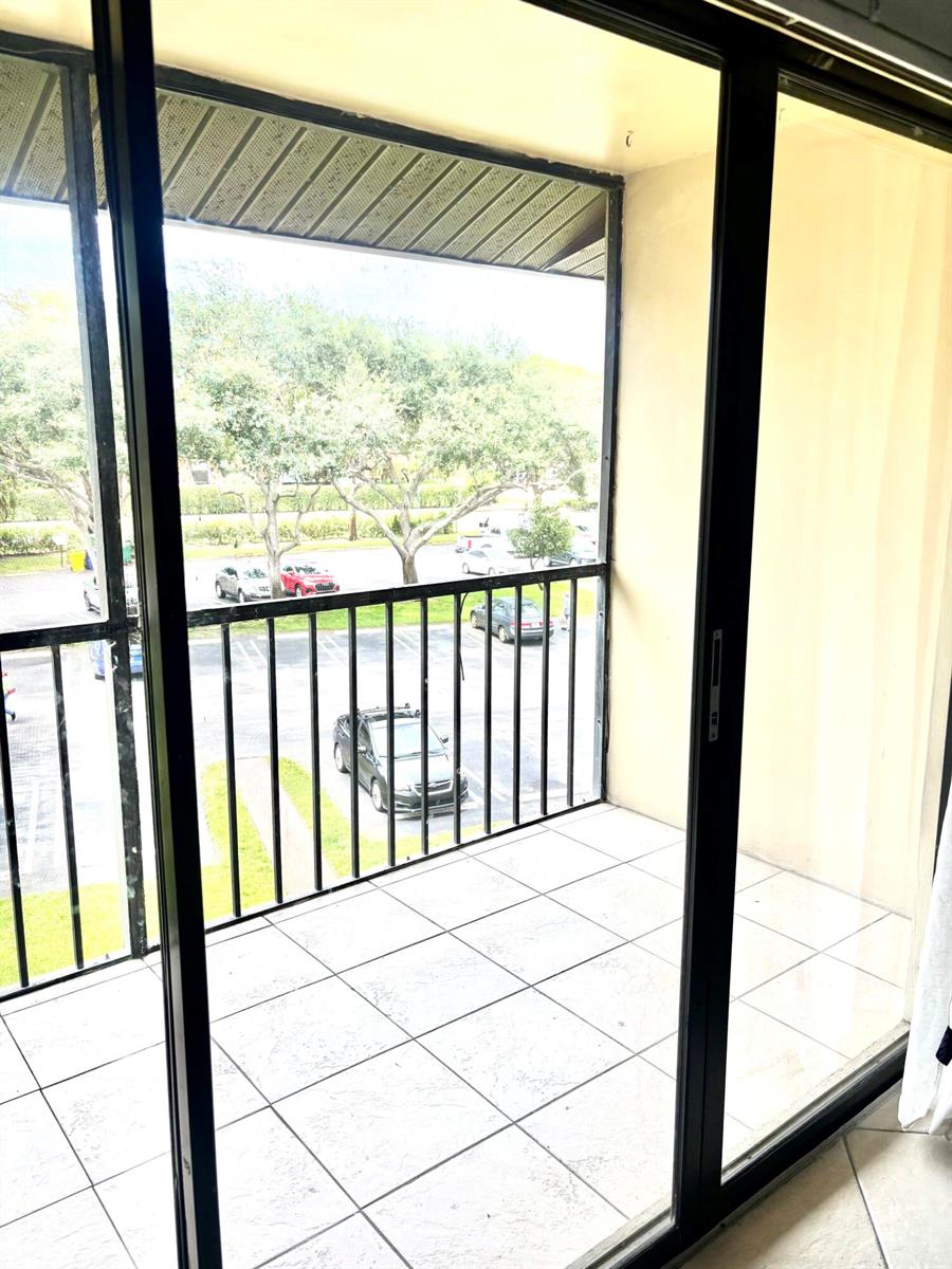 A balcony with white tile flooring and a black metal railing overlooks a parking lot — 201 Foxtail Drive # H3, FL 33415, FL