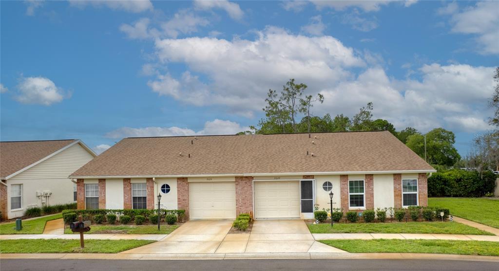A single-story duplex with brick accents, two garage doors, and a brown shingled roof — 9022 RAMSGATE DRIVE UNIT 9022, NEW PORT RICHEY, FL