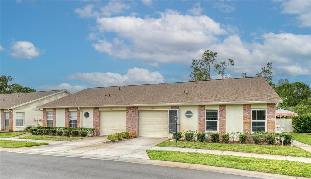 A single-story duplex with beige stucco walls, brick accents, and two attached garages — 9022 RAMSGATE DRIVE UNIT 9022, NEW PORT RICHEY, FL