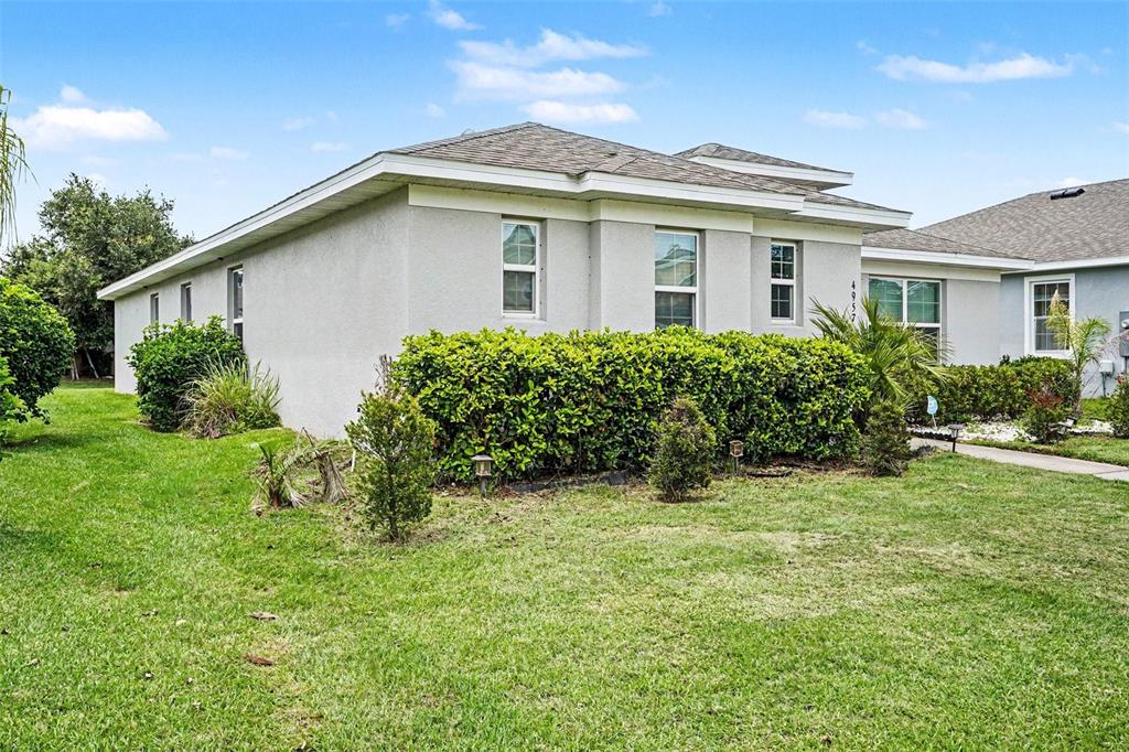 A single-story house with a gray stucco exterior, a shingled roof, and a manicured hedge — 4957 CASTLE STREET E, KISSIMMEE, FL