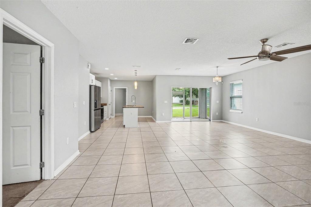 An open-concept living area features light-colored tile flooring, a kitchen island, and sliding glass doors — 4957 CASTLE STREET E, KISSIMMEE, FL