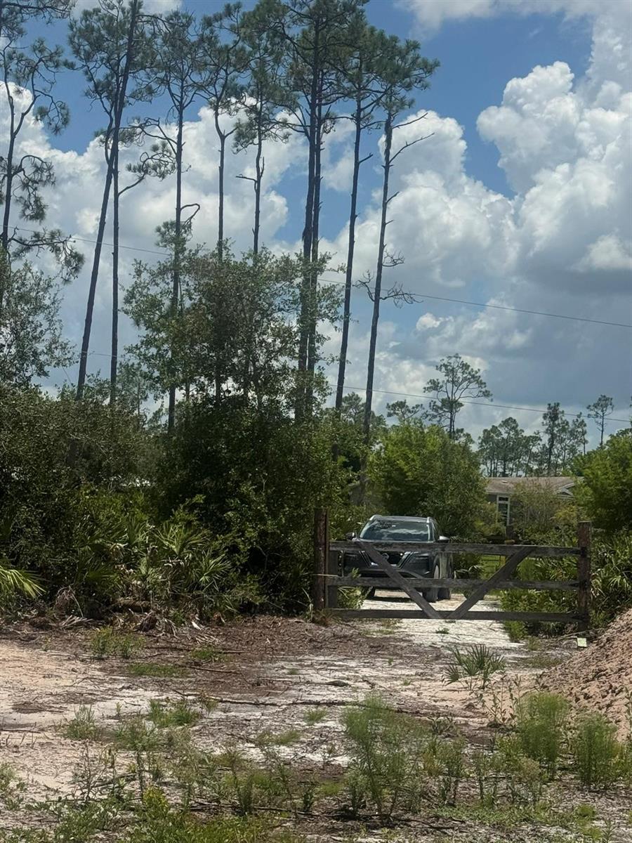 A wooden gate stands at the entrance of a sandy driveway leading to a parked car — 32801 Highway 441, Okeechobee FL 34972, OKEECHOBEE, FL