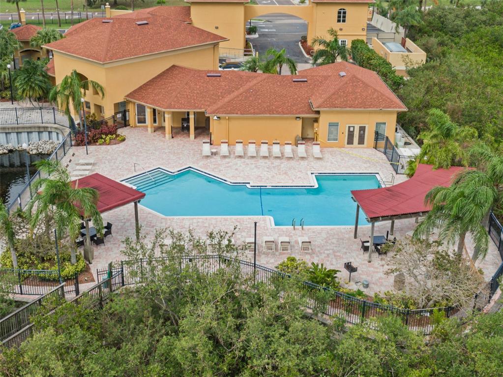 An aerial view of a community swimming pool with lounge chairs and two shaded cabanas — 4305 BAYSIDE VILLAGE DRIVE UNIT 104, TAMPA, FL