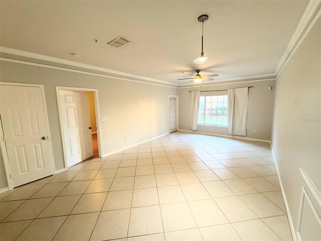A spacious room with light-colored tile flooring, crown molding, a ceiling fan, and a window — 4305 BAYSIDE VILLAGE DRIVE UNIT 104, TAMPA, FL