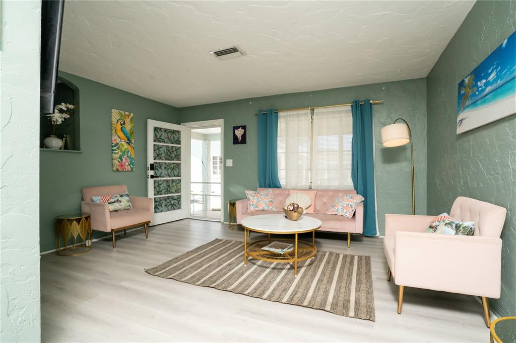 A living room features sage green walls, light wood flooring, pink furniture, and a rug — 5029 28TH AVENUE S, GULFPORT, FL