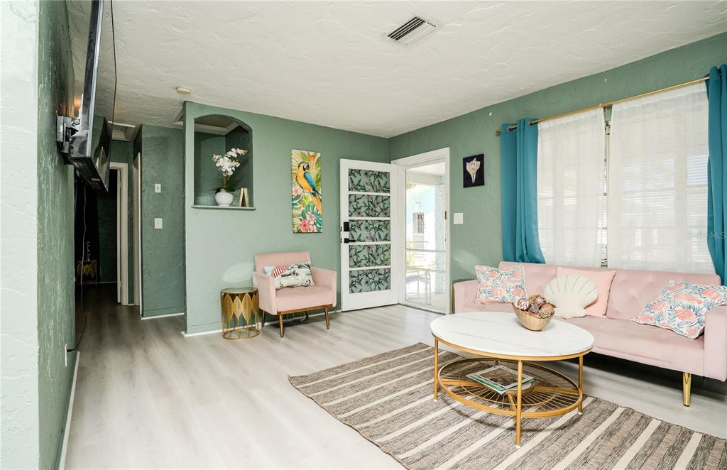 A living room features sage green walls, a pink sofa, light wood floors, and a rug — 5029 28TH AVENUE S, GULFPORT, FL