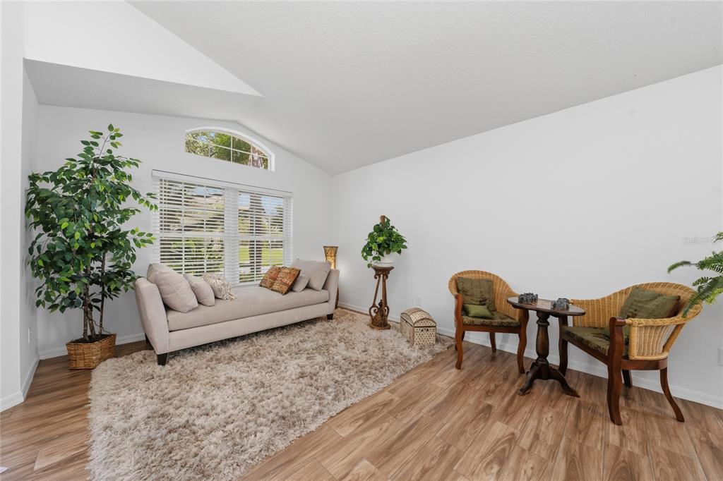 A living room with wood-look flooring, a beige sofa, two wicker chairs, and a shag rug — 13613 BUDWORTH CIRCLE, ORLANDO, FL