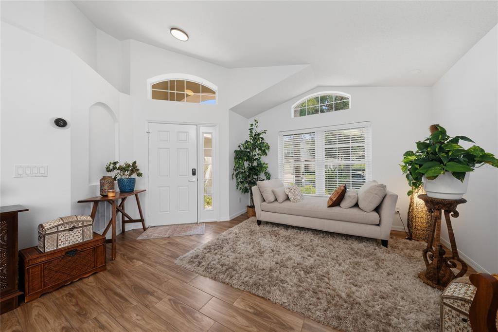 A bright living room features white walls, wood-look flooring, a beige sofa, and arched windows — 13613 BUDWORTH CIRCLE, ORLANDO, FL
