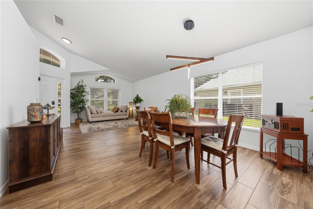 A dining room with wood-look tile flooring, a wooden table, and an adjacent living area — 13613 BUDWORTH CIRCLE, ORLANDO, FL