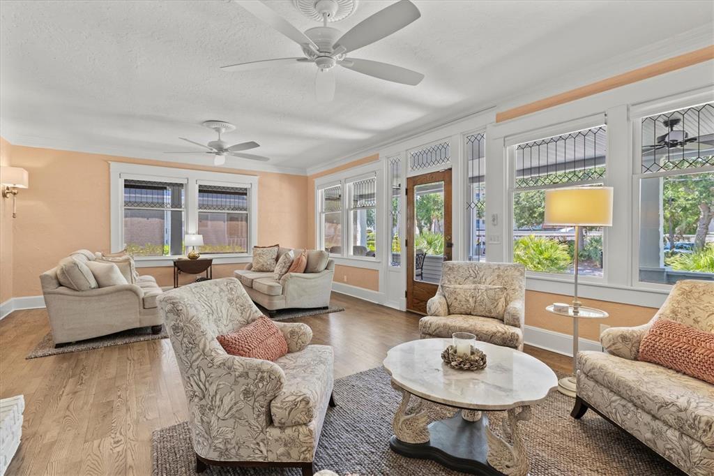 A sunroom features light peach walls, hardwood floors, two ceiling fans, and multiple seating areas — 1523 1ST AVENUE W, BRADENTON, FL