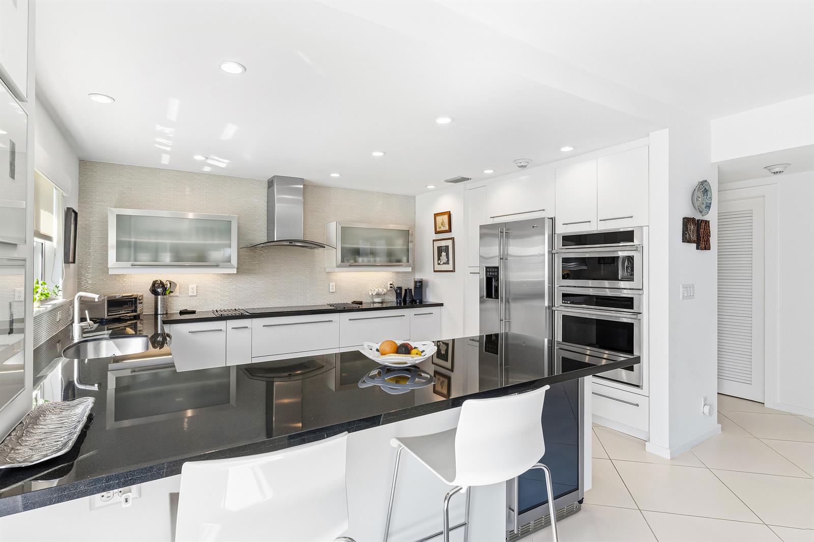 A modern kitchen features white cabinetry, black granite countertops, stainless steel appliances, and a central island — 200 Macfarlane Drive # 406, Delray Beach FL 33483, DELRAY BEACH, FL