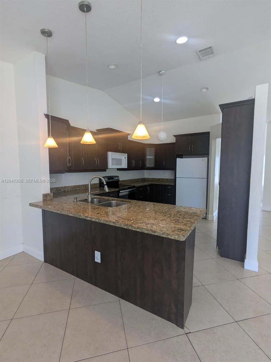 A kitchen features dark wood cabinets, granite countertops, a breakfast bar, and pendant lighting — 12335 SW 193rd St # 12335, Miami FL 33177, MIAMI, FL