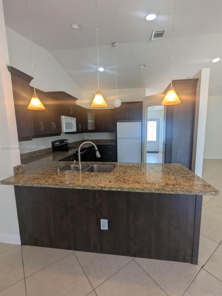 A kitchen features dark wood cabinets, granite countertops, a stainless steel sink, and pendant lighting — 12335 SW 193rd St # 12335, Miami FL 33177, MIAMI, FL