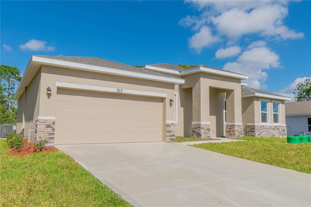 A tan single-story house with a two-car garage and stone accents under a blue sky — 913 SANGER STREET SE, PALM BAY, FL