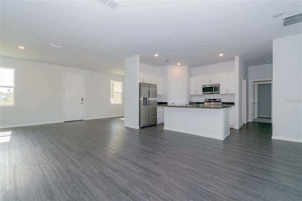 A modern open-concept kitchen features white cabinetry, stainless steel appliances, and gray wood-look flooring — 913 SANGER STREET SE, PALM BAY, FL
