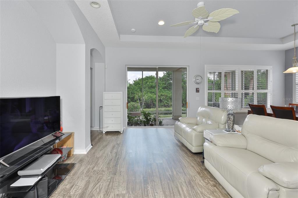 A living room with light wood-look flooring, white leather furniture, and sliding glass patio doors — 1050 REGAL MANOR WAY, SUN CITY CENTER, FL