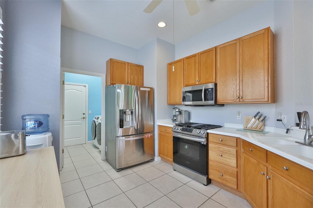 A kitchen features light wood cabinets, stainless steel appliances, and a doorway leading to laundry — 1050 REGAL MANOR WAY, SUN CITY CENTER, FL